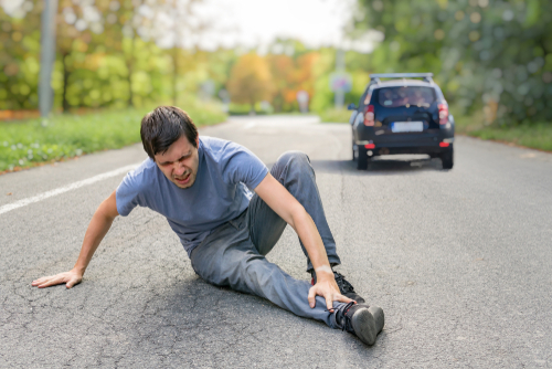 Injured man on road in front of a car.