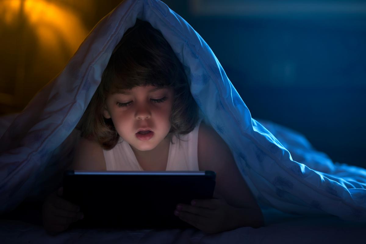 Child watching a tablet under a blanket