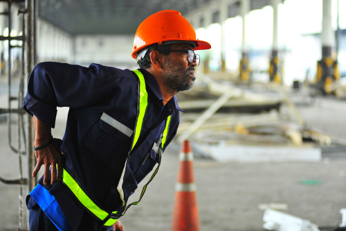 Senior worker with backache at construction site in warehouse.