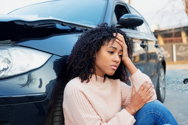 Woman sitting against car following accident with head in hands